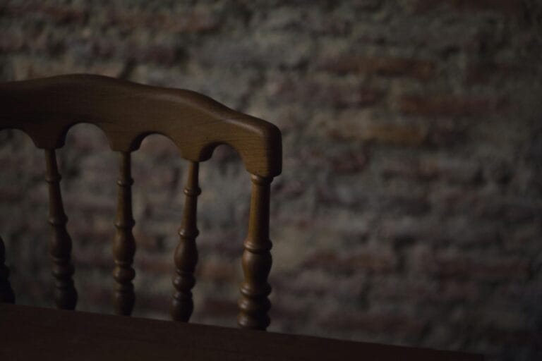 Close-up of an antique wooden chair with a textured, rustic brick wall background.
