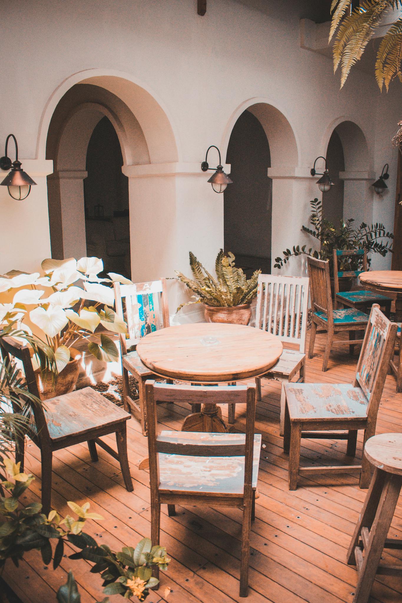 Inviting indoor patio with rustic wooden chairs and tables, surrounded by lush plants and elegant arches.